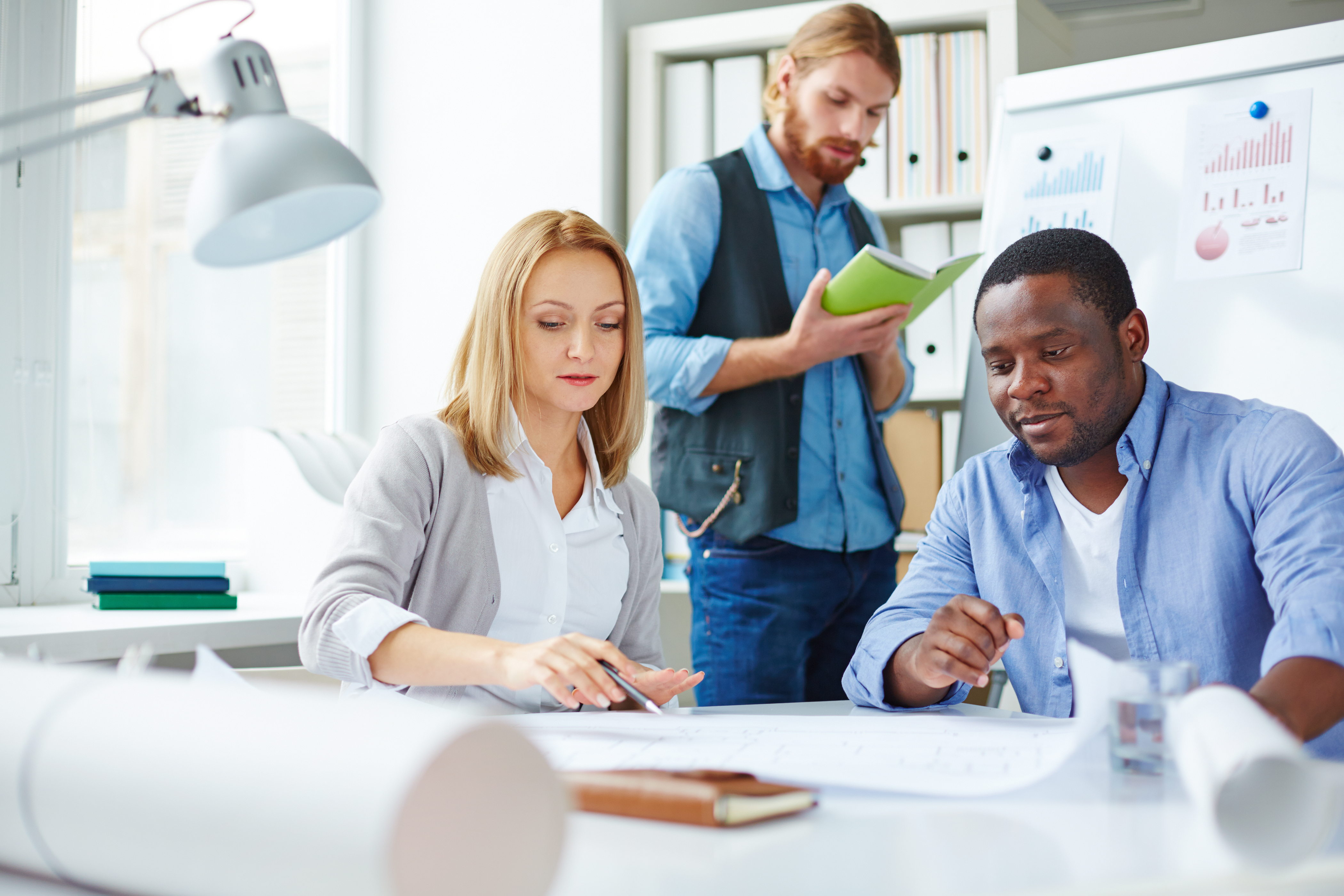 Blond businesswoman pointing at blueprint with her colleagues near by
